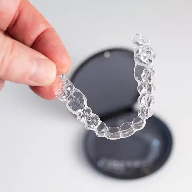 Clear aligners held by hand, showing transparent orthodontic treatment device over dark base.